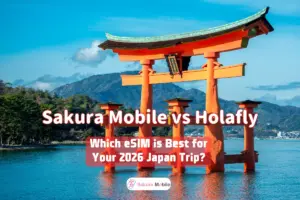 Itsukushima Shrine floating torii gate in Miyajima, Japan, standing in the water with mountains in the background under a clear, blue sky.