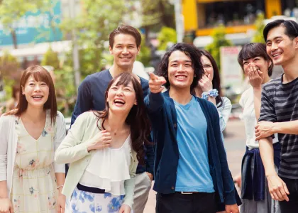 A group of 6 friends, all smiling while on an outing in an open space in Japan.