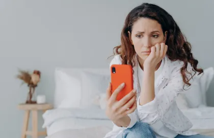 A woman troubled while looking at various phone plans on her orange smartphone.