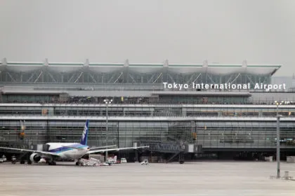 Exterior view of the Tokyo International Airport (Haneda) terminal building iwth an All Nippon Airways (ANA) plane parked on the tarmac.