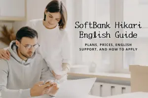 Smiling couple in a kitchen comparing information on a smartphone and laptop with moving boxes nearby.