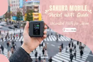 A hand holding a Sakura Mobile device in fornt of a busy Shibuya Scramble.