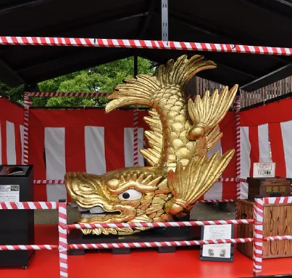 Close-up photo of golden sachihoko statue displayed in exhibition booth draped with red and white striped banners