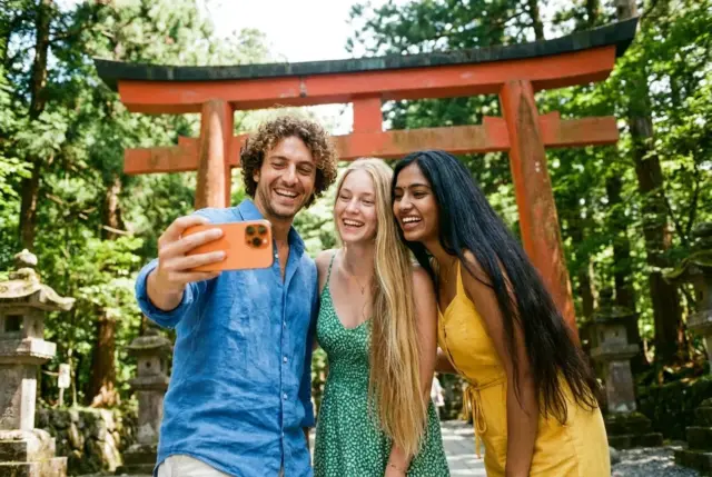 Friends taking a selfie by a shrine gate in the forests of Nikko.