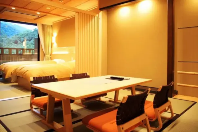 Warmly lit ryokan guest room featuring a low Japanese-style dining table and a Western-style bed.