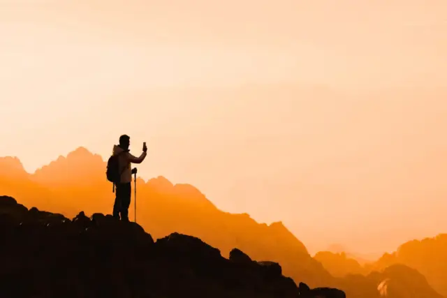 Hiker taking a photo with a smartphone on a mountain trail.