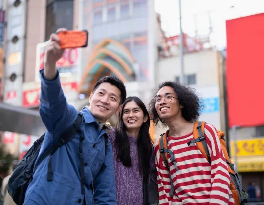 Tourists take a selfie with their smartphone while walking around a shopping district in Japan.